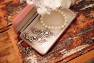 A close-up of luxurious pearls and intricate earrings in an open jewelry box on a rustic wooden table.
