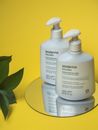 Close-up of skincare foamy soap-free cream bottles on a mirror with a yellow backdrop.