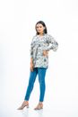 Elegant woman wearing floral tunic, blue jeans, and heels on a white background.