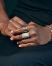 Close-up of crossed hands with elegant silver rings and bracelet against a dark fabric background.