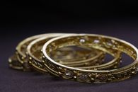 Elegant close-up of ornate gold bangles with gemstone accents on a dark surface.